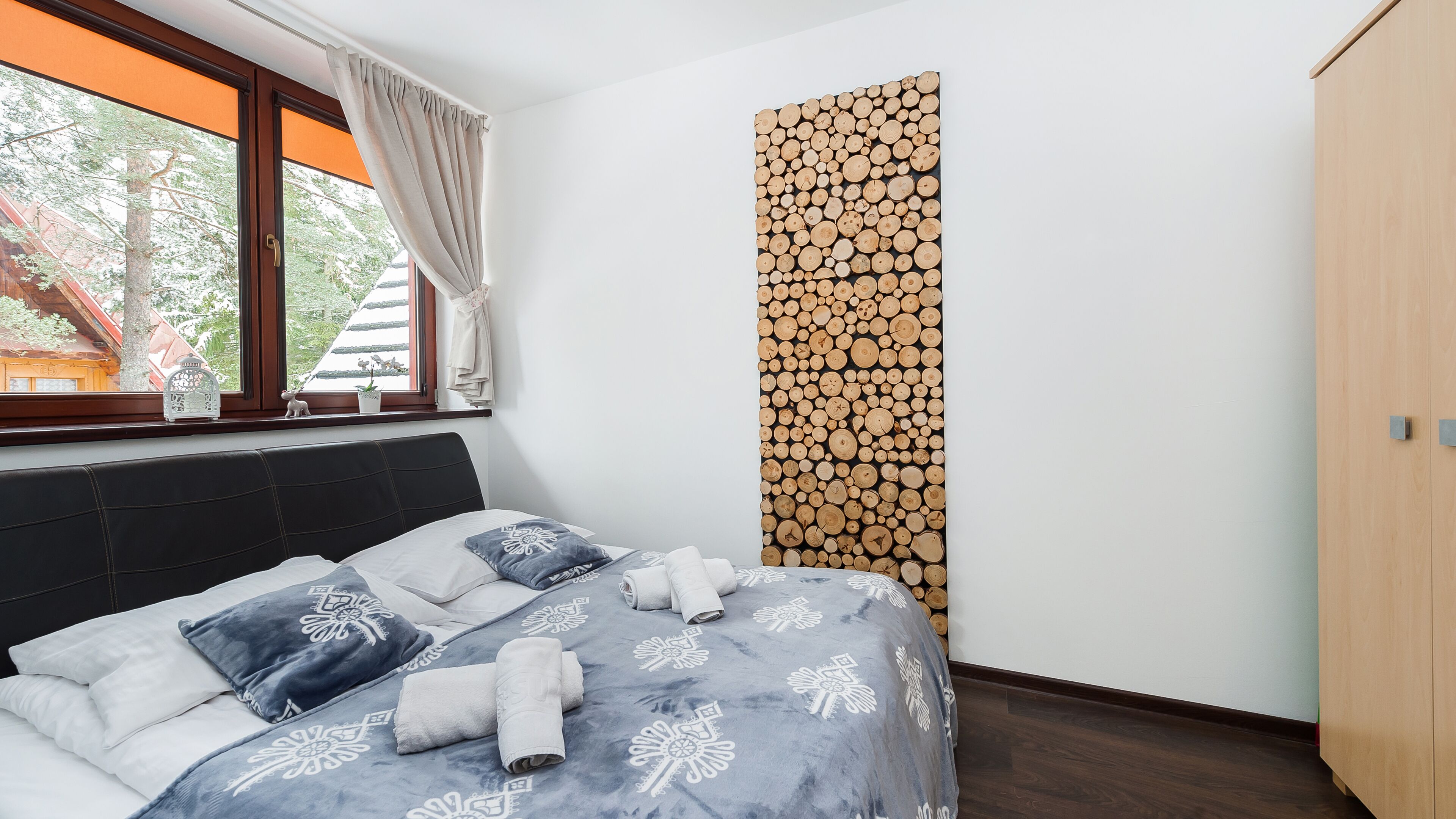 Ein Schlafzimmer mit Bett, Fenster mit Vorhängen, einer Wand mit Holzmuster und einem Holzschrank.