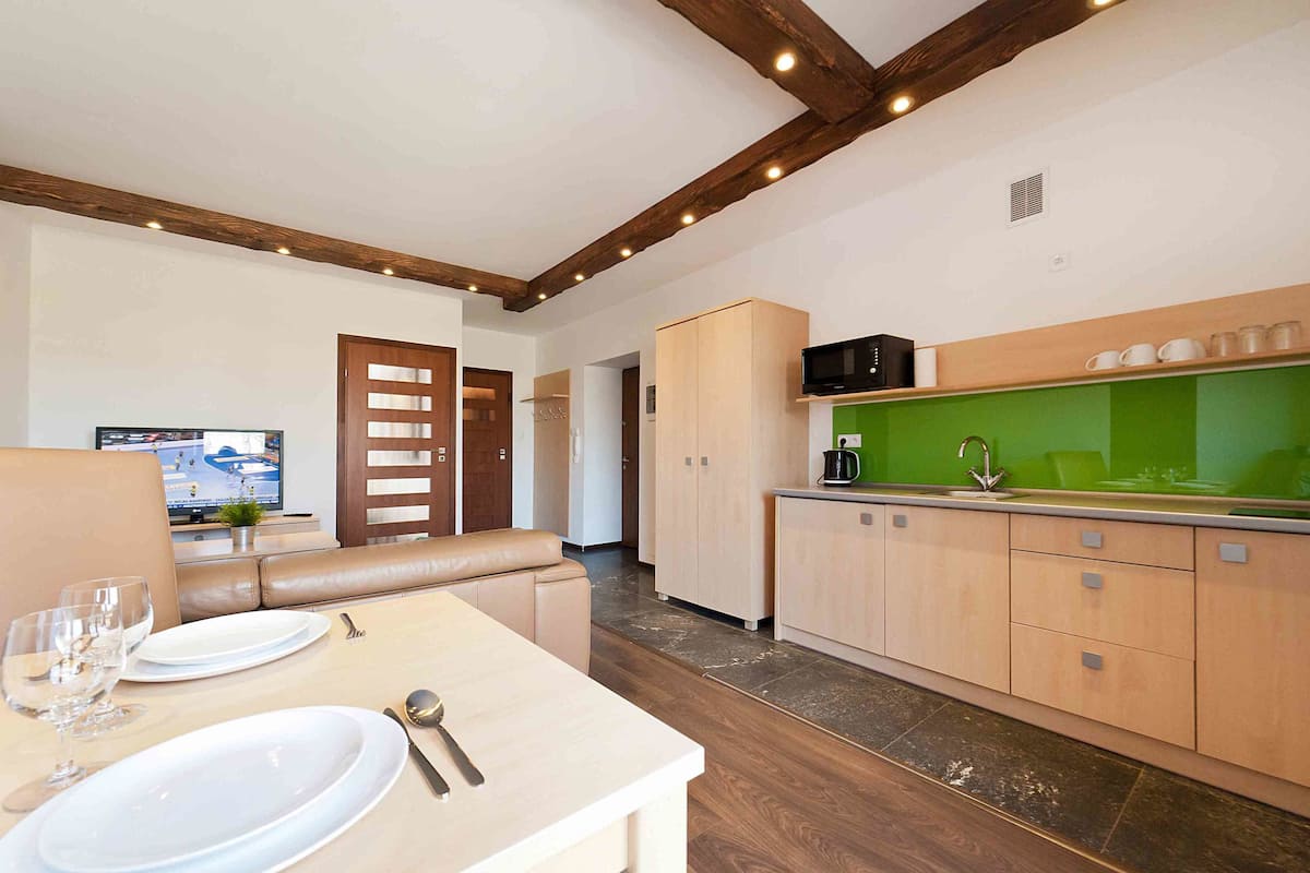 Een moderne keuken met houten kastjes, een groen aanrecht en een eethoek met een tafel gedekt voor twee personen.