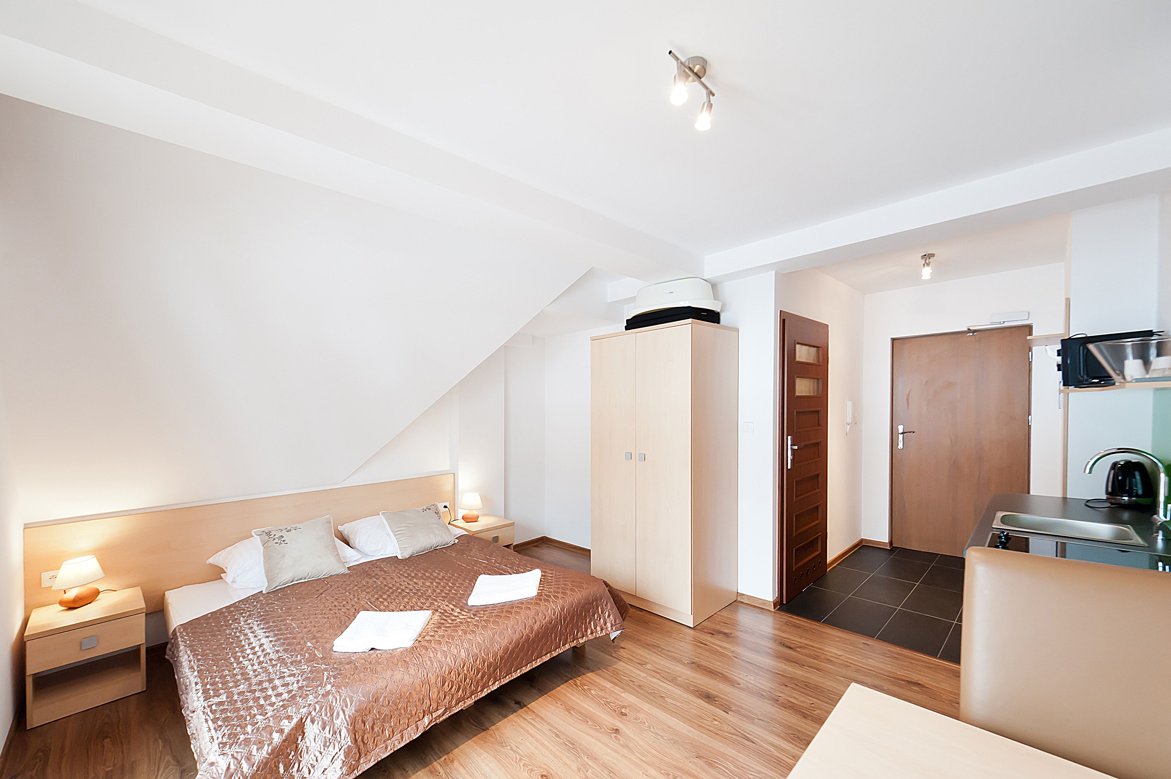 A modern bedroom with a bed, bedside tables, a wardrobe, and a kitchenette area.