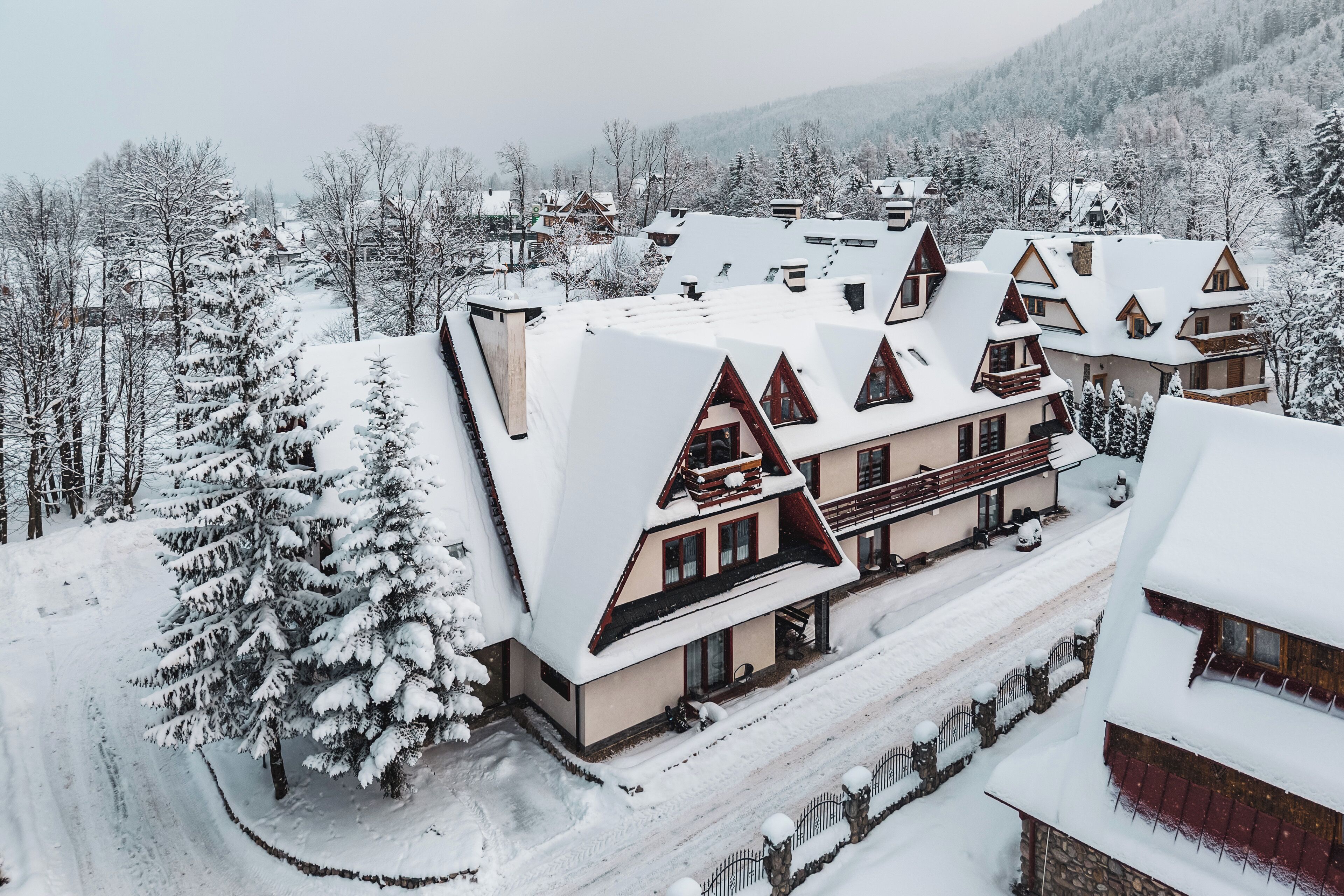 Un bâtiment enneigé, doté de nombreux balcons et d’un toit à forte pente, entouré d’arbres chargés de neige et se dressant sur un fond de montagnes.