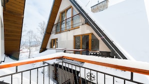 A two-story chalet with a balcony, wooden railings, and a stone facade. - Apartamenty Sun & Snow Poronin (Bialy Dunajec)