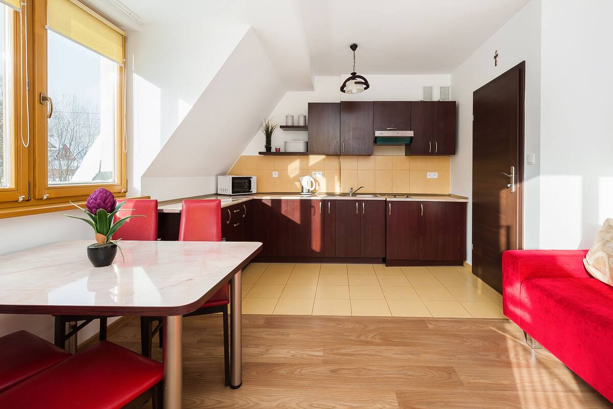 Een moderne keuken met donkere houten kasten, een rode eethoek met een tafel en stoelen, en een rode bank.