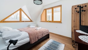 A bedroom with a bed, a desk, and two windows with wooden frames. - Apartamenty Sun & Snow Poronin (Bialy Dunajec)