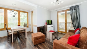 A modern living room with a wooden dining table, a sofa, and a TV on a cabinet. - Apartamenty Sun & Snow Poronin (Bialy Dunajec)