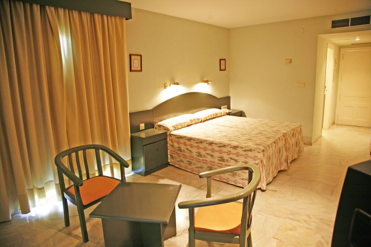 A hotel room with a bed, two bedside tables, a desk with a chair, and a curtain.