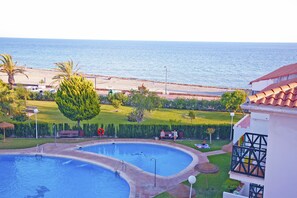 A swimming pool with a view of the sea, a beach, and a grassy area with benches. - ELE La Perla (Motril)