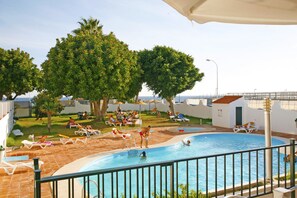 A pool area with lounge chairs and a swimming pool, surrounded by trees and a clear sky. - ELE La Perla (Motril)