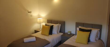 A hotel room with two beds, each with a headboard, bedside tables, lamps, and towels.
