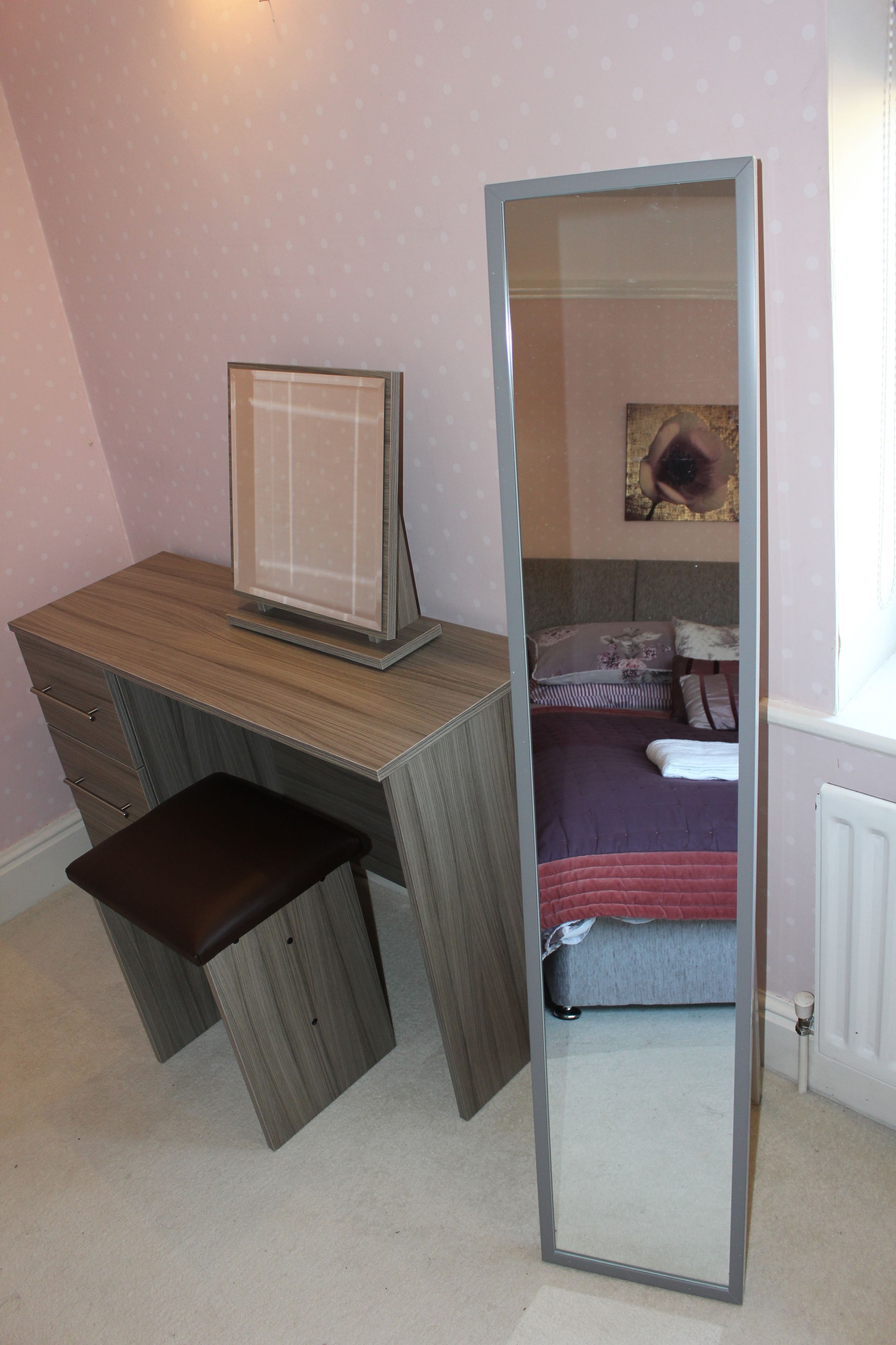 A bedroom with a bed, a desk, and a mirror.