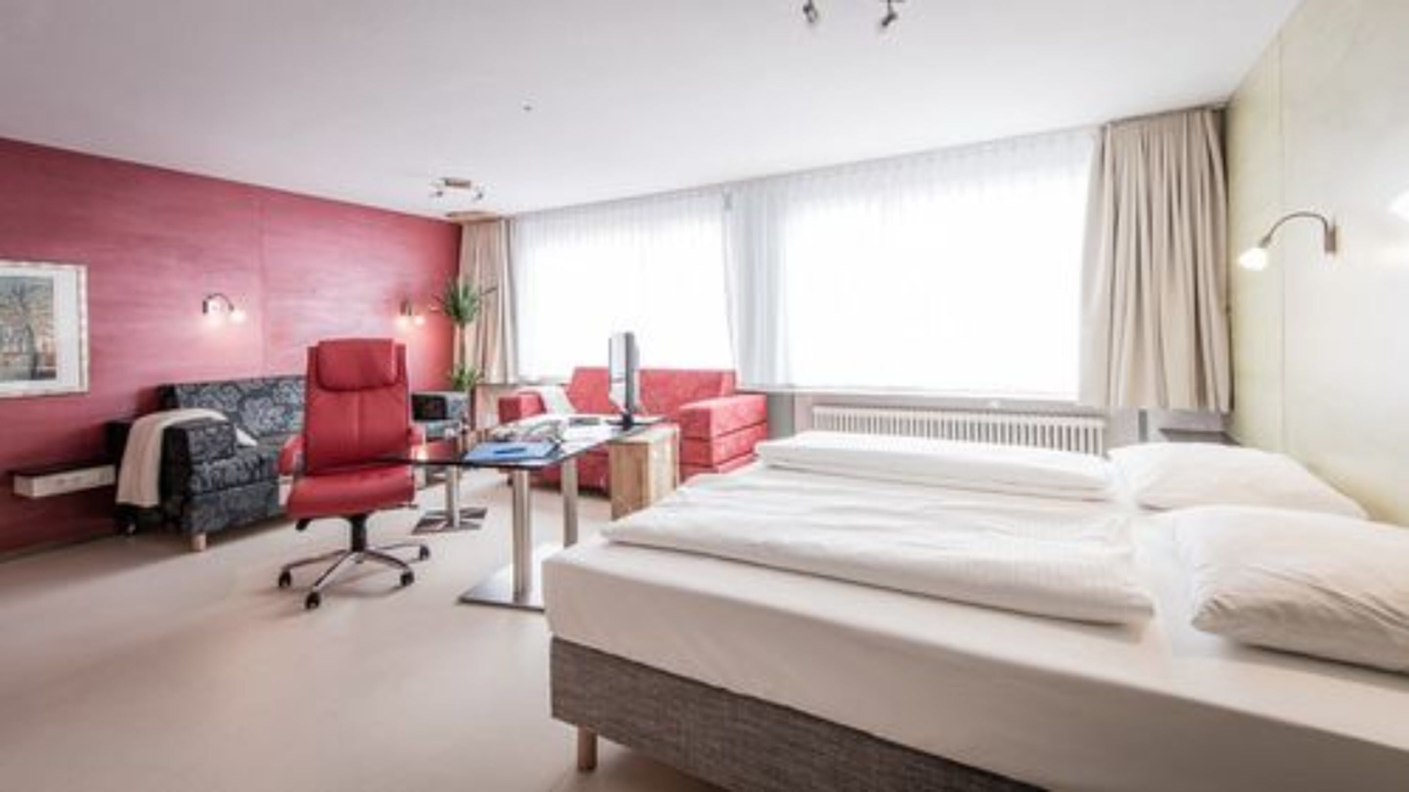 Une chambre d’hôtel avec un lit, un fauteuil rouge, un bureau et un canapé.