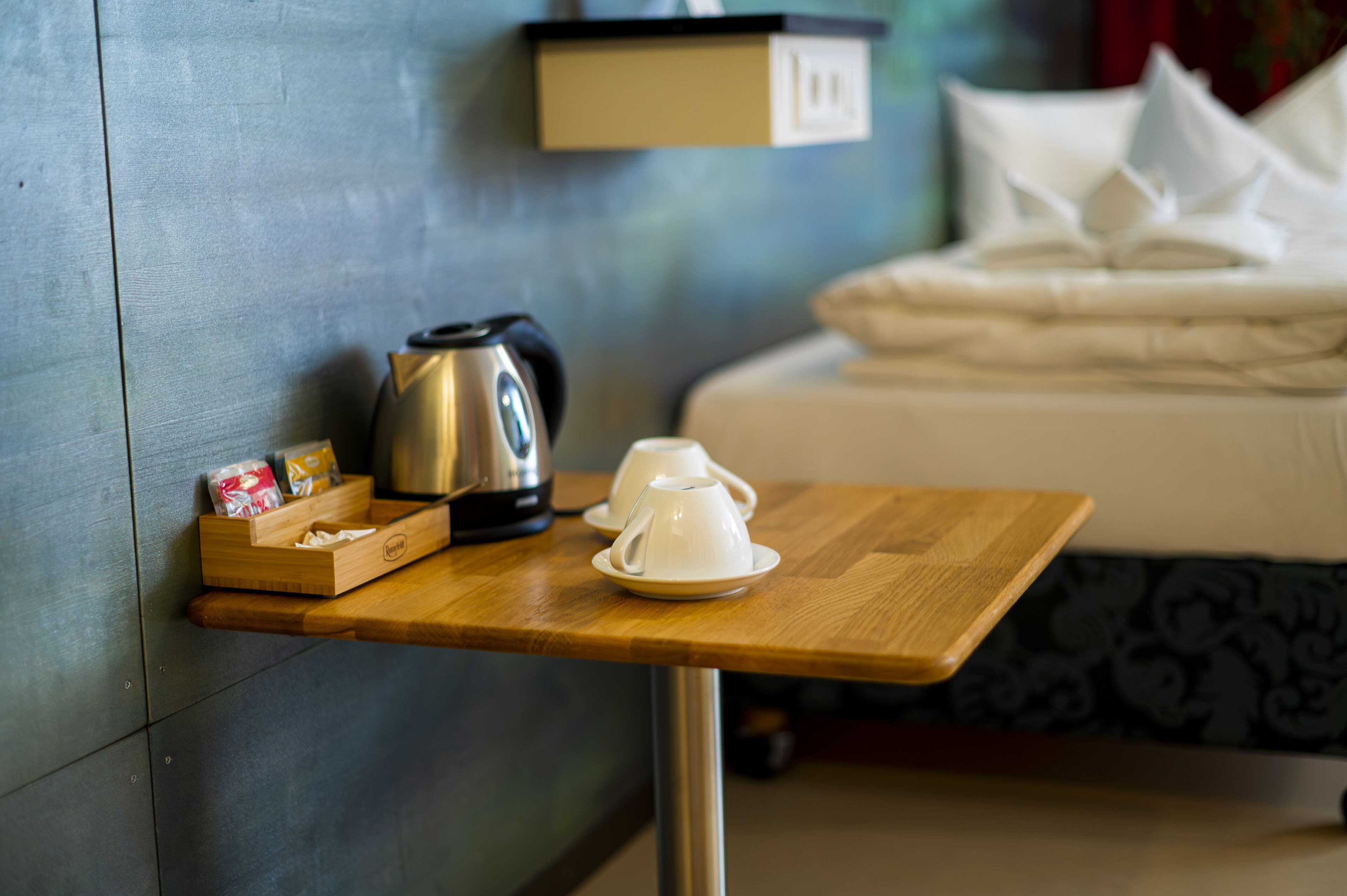 Une table en bois avec une tasse blanche et une bouilloire, une boîte de mouchoirs et un présentoir à mouchoirs.