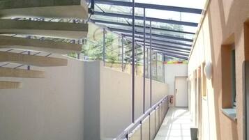 A covered outdoor corridor with a metal railing, a staircase, and a door at the end.