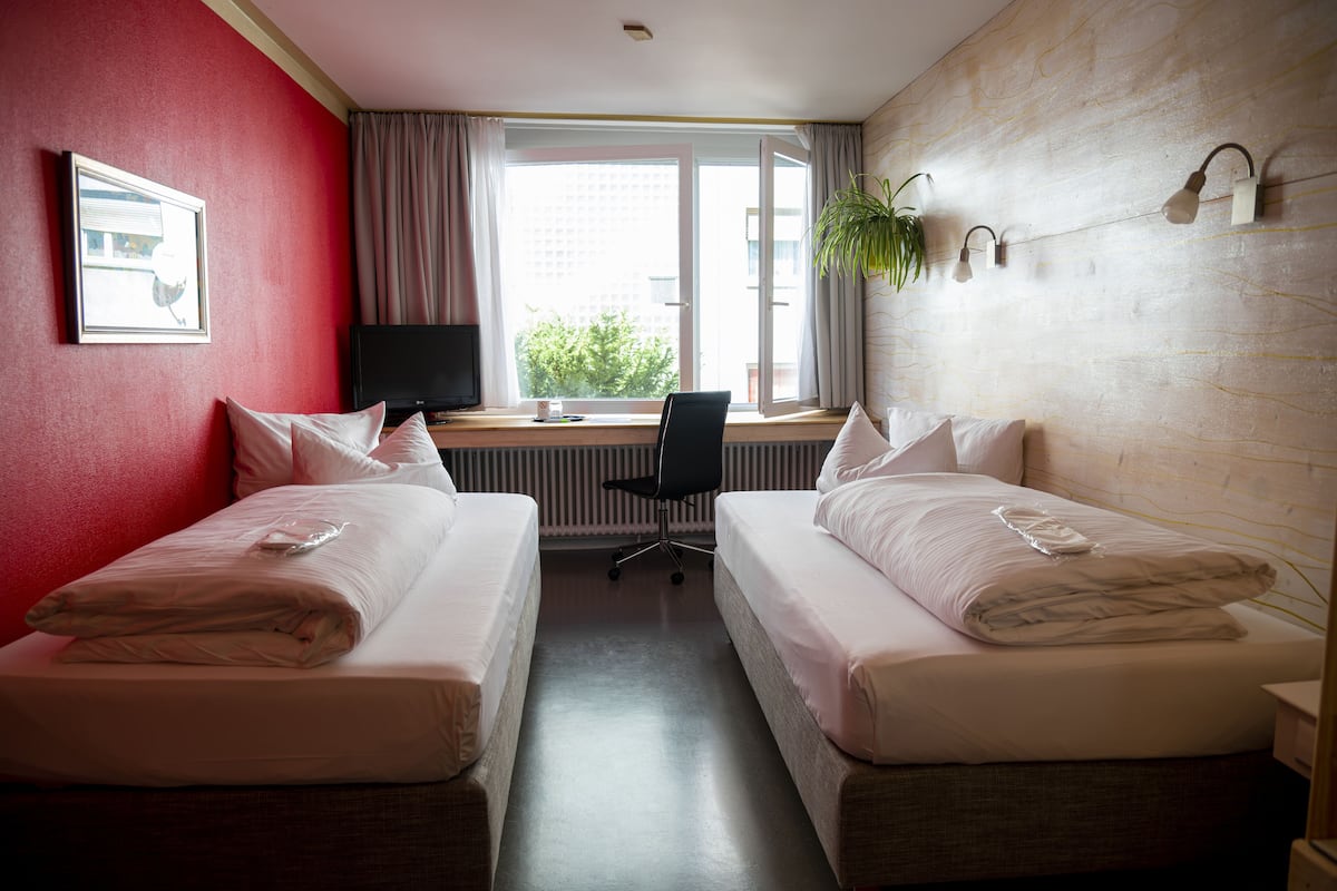 Habitación de hotel con dos camas, un escritorio con computadora, una silla y una ventana con cortinas.