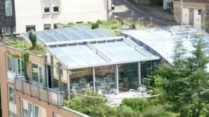 Un edificio moderno con jardín en la azotea y una estructura de invernadero de vidrio.
