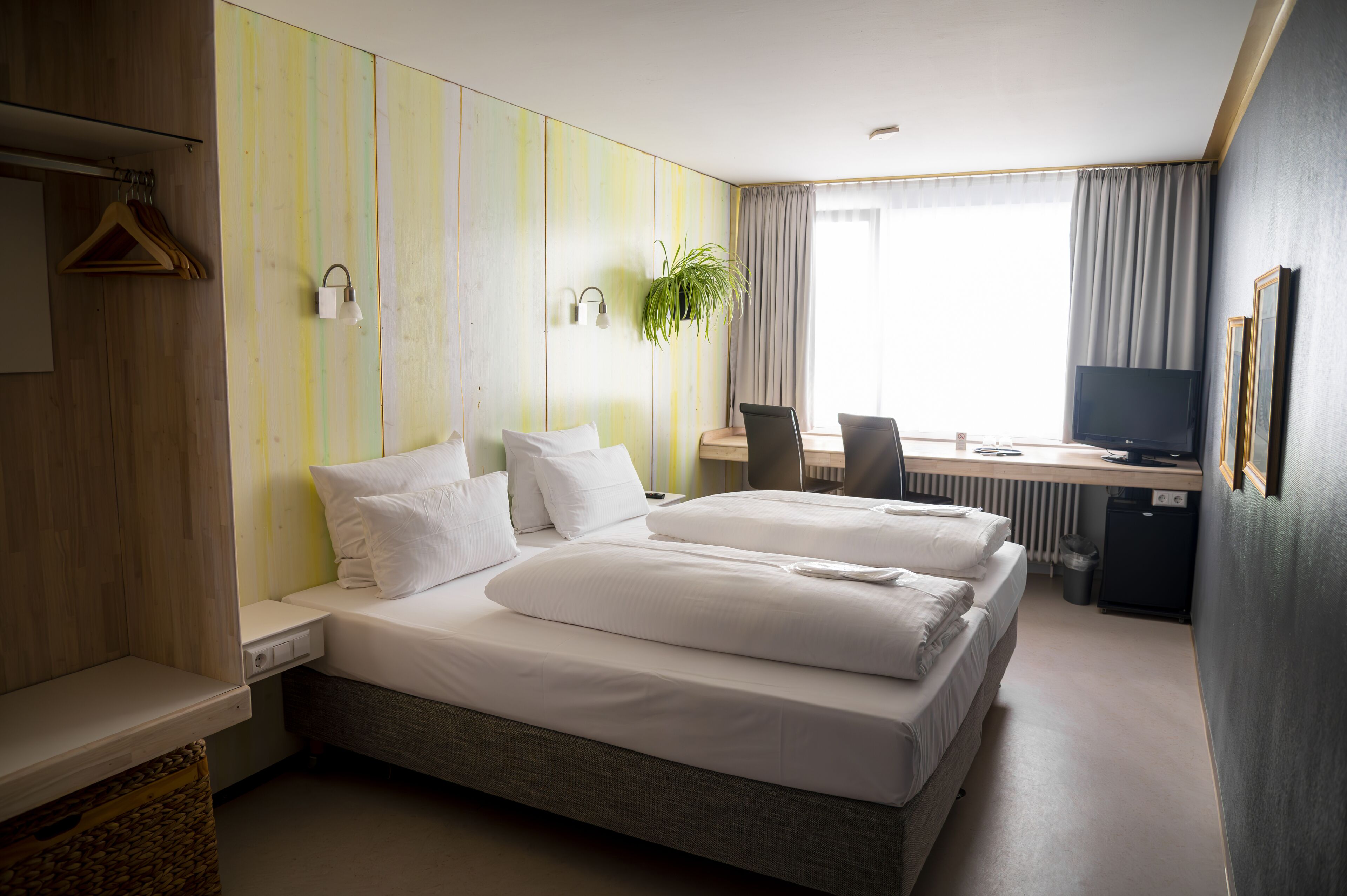 A hotel room with a large bed, a desk with a computer, a television, and a plant.