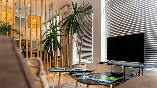 Una sala de estar moderna con un televisor de pantalla plana, decoración de bambú y un amplio ventanal con persianas.