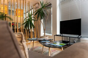 A modern living room with a flat-screen TV, bamboo decor, and a large window with blinds. - Central Guest House (Ponta Delgada)