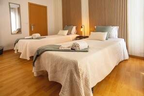 A hotel room with two beds, wooden flooring, a mirror, and a wall-mounted light fixture. - Central Guest House (Ponta Delgada)