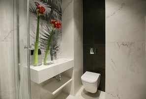 A modern bathroom with a white sink, two glass vases with red flowers, a toilet, and a dark tiled wall.