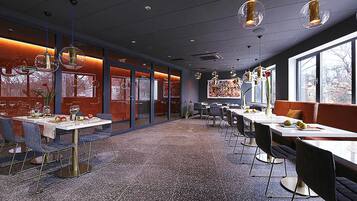 A modern dining area with tables and chairs, large windows, and hanging pendant lights.