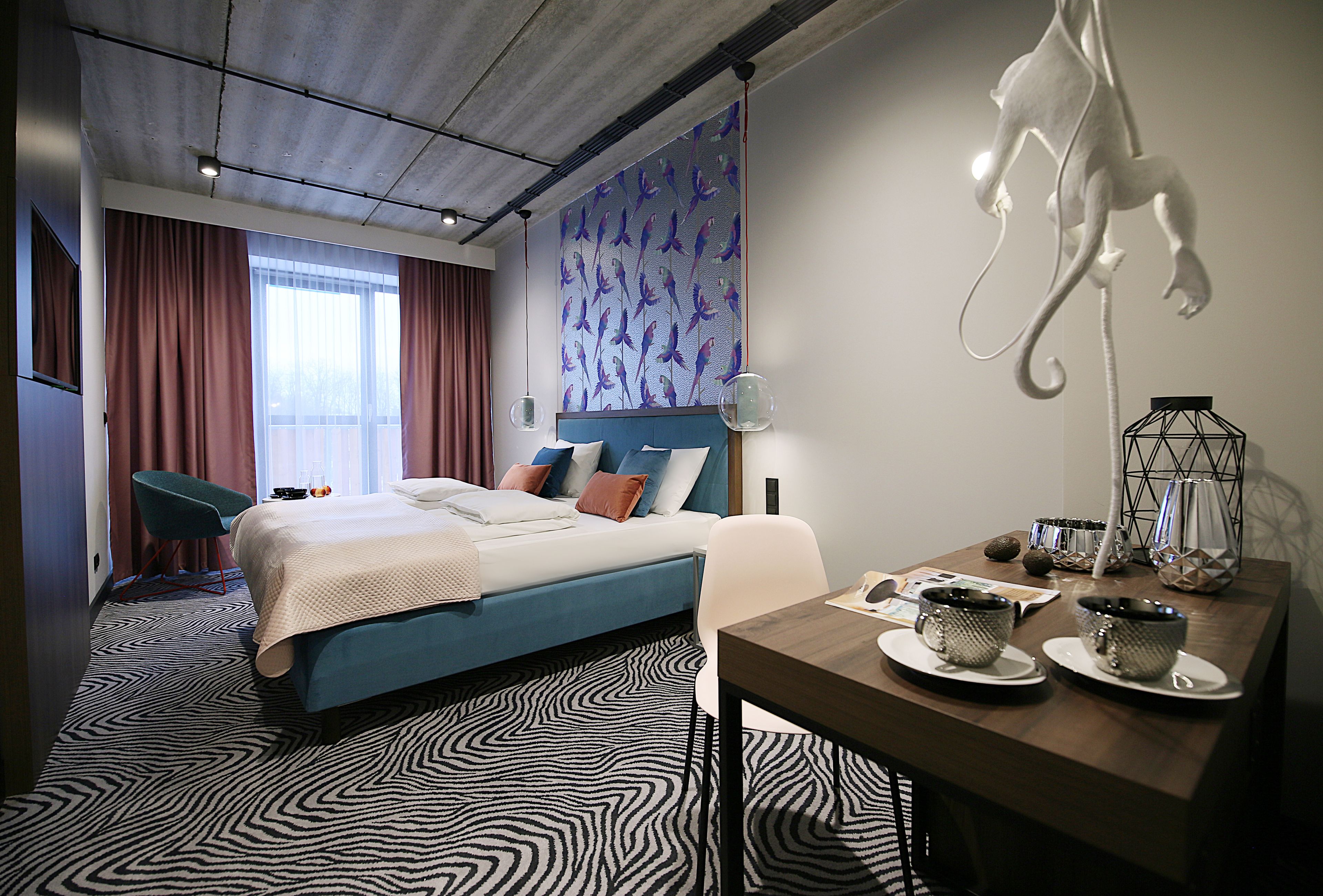 Una habitación de hotel con una cama, un escritorio con lámpara, una silla y una alfombra con estampado de cebra.