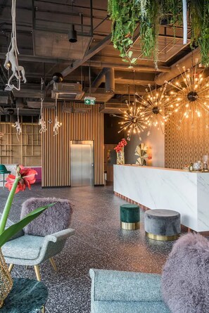 A modern reception area with a marble counter, hanging plants, and a unique ceiling light fixture.