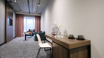 A modern hotel room with a wooden desk, a chair, a sofa, and a patterned carpet.