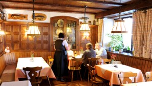A cozy restaurant with wooden paneling, tables with white tablecloths, and hanging lamps. - Hotel Restaurant Pension Krone Post (Simonswald)