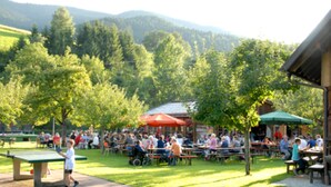 An outdoor dining area with tables and chairs, surrounded by trees and a mountain backdrop. - Hotel Restaurant Pension Krone Post (Simonswald)