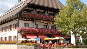 A traditional building with a balcony adorned with flowers, outdoor seating, and a visible parking sign. - Hotel Restaurant Pension Krone Post (Simonswald)