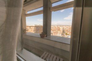 A balcony with a potted plant, a wooden bench, and a view of a cityscape with buildings and mountains in the distance. - Bed a Catania (Catania)
