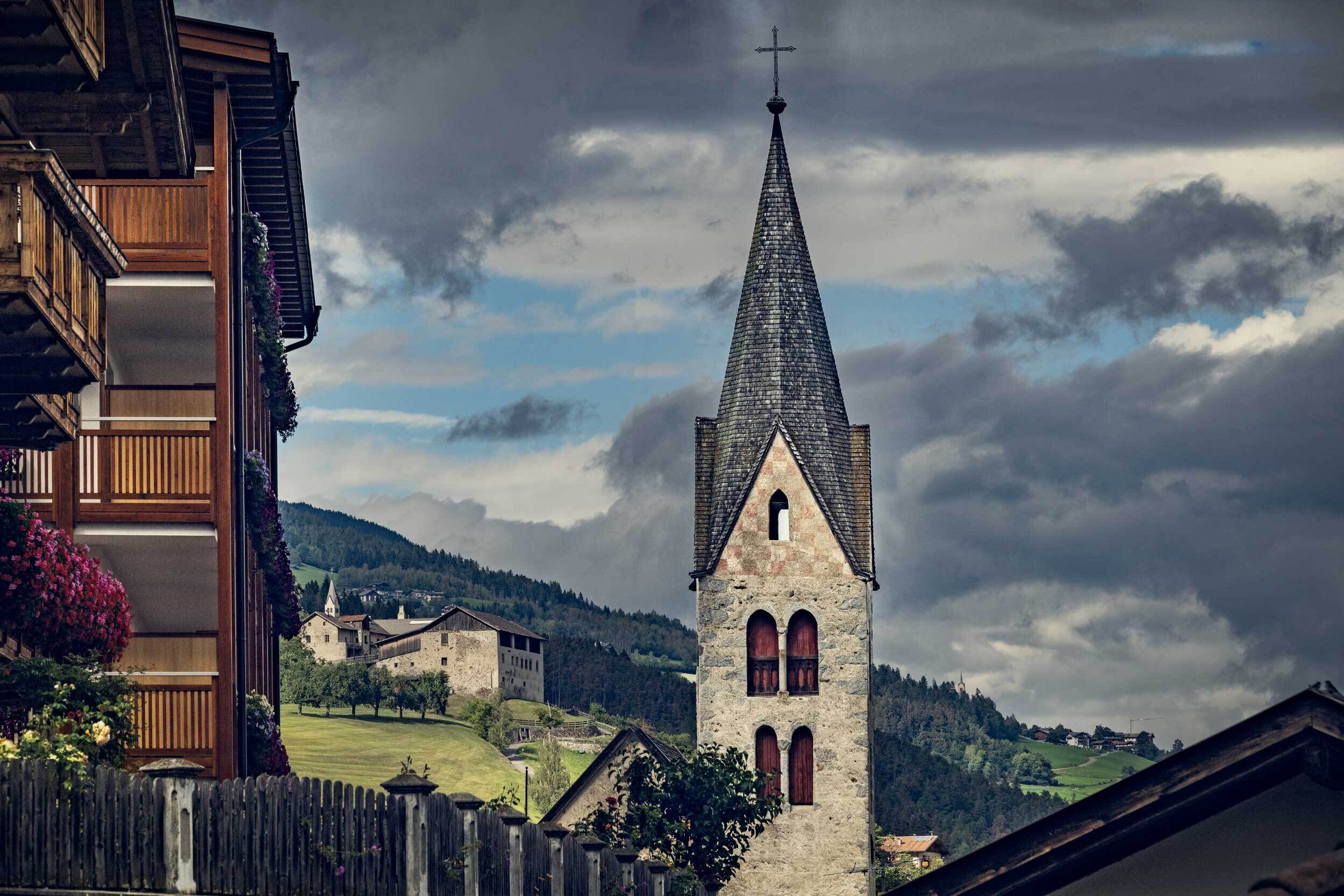 Una iglesia con un campanario alto, rodeada de edificios tradicionales y un paisaje rural.