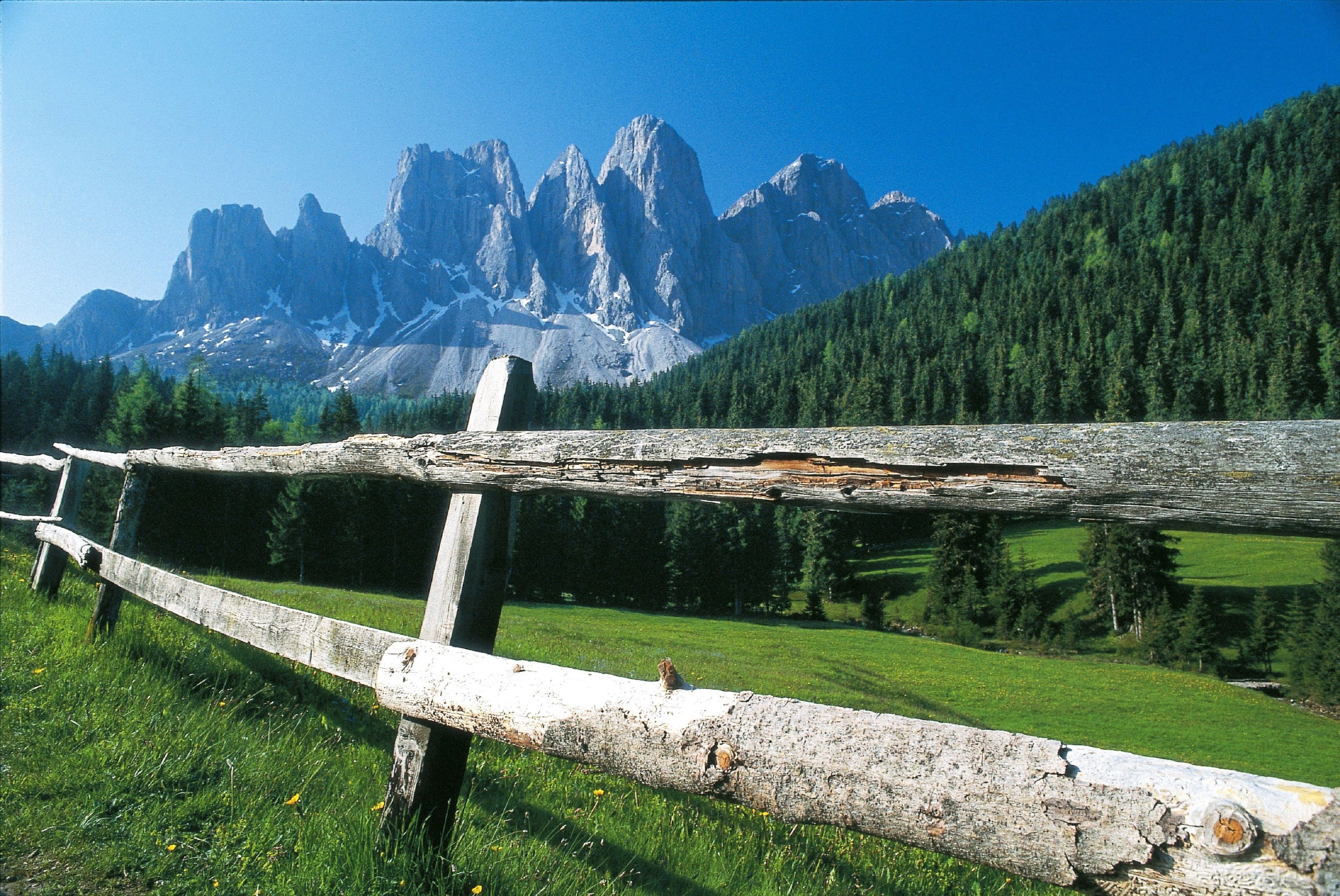A rustic wooden fence in a mountainous landscape with a clear view of rugged peaks in the background.