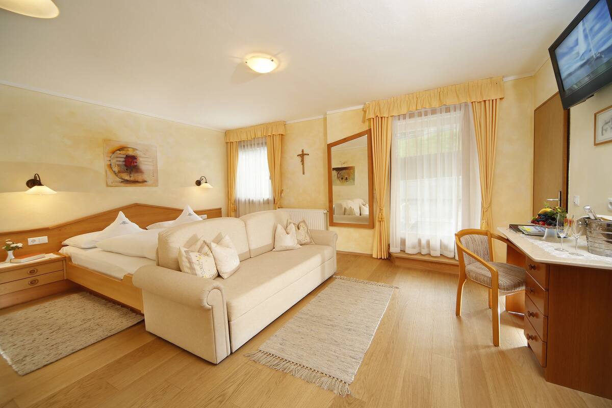 A hotel room with a bed, a sofa, a desk, a chair, a TV, and a window with curtains.