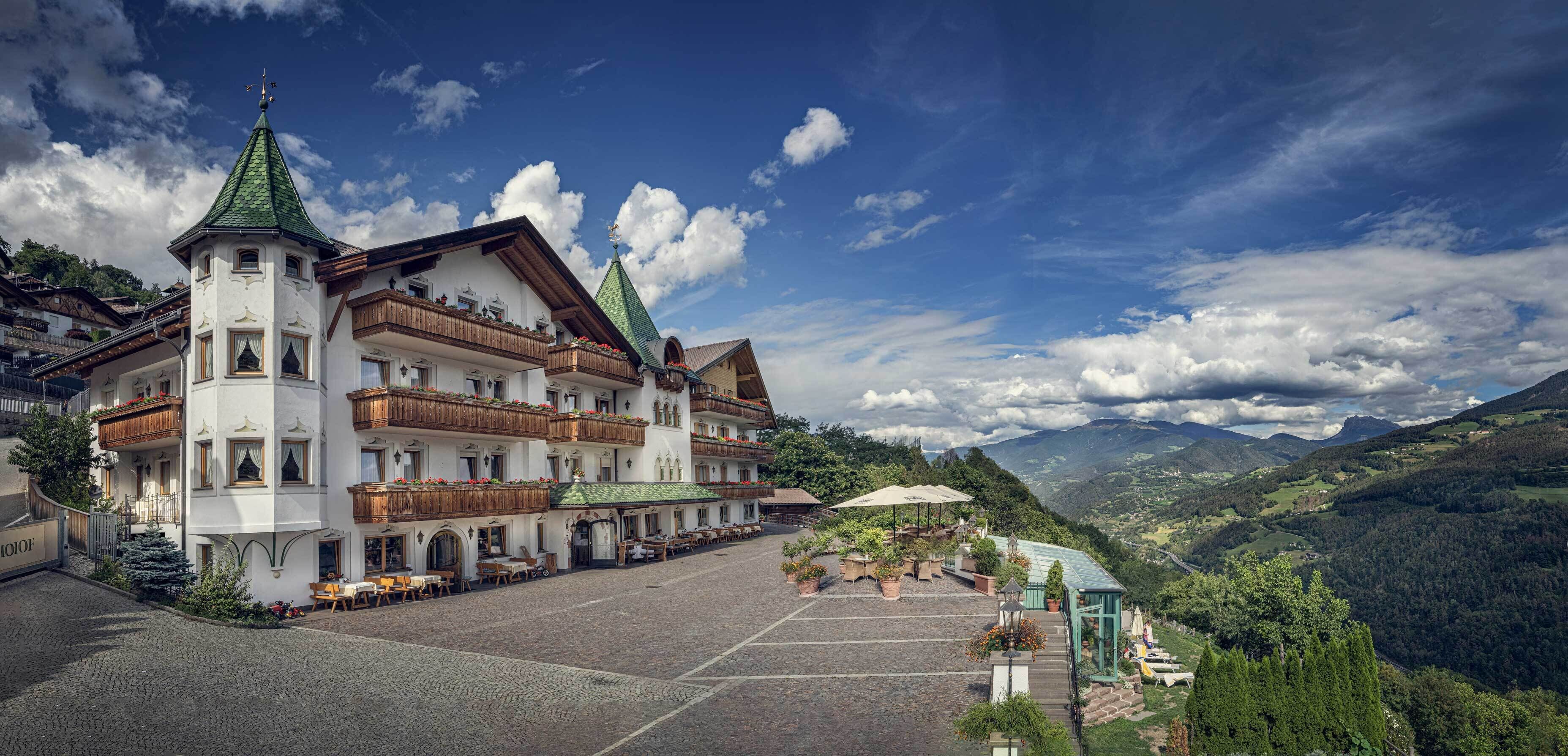 Un hotel europeo tradicional con varios balcones, un patio central y vistas a la montaña.