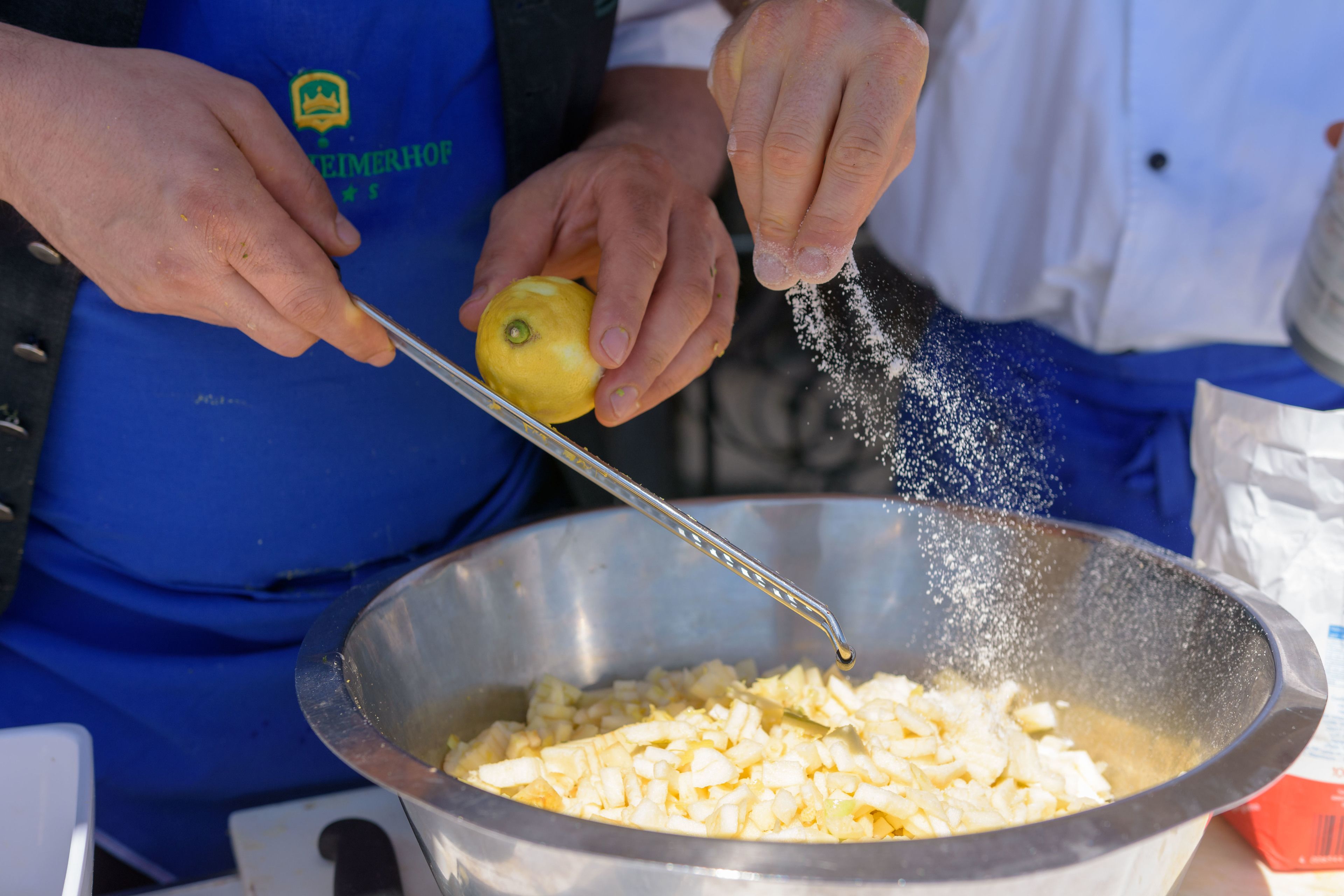 Une personne préparant de la nourriture, plus précisément en râpant du zeste de citron au-dessus d’un bol de fromage râpé.