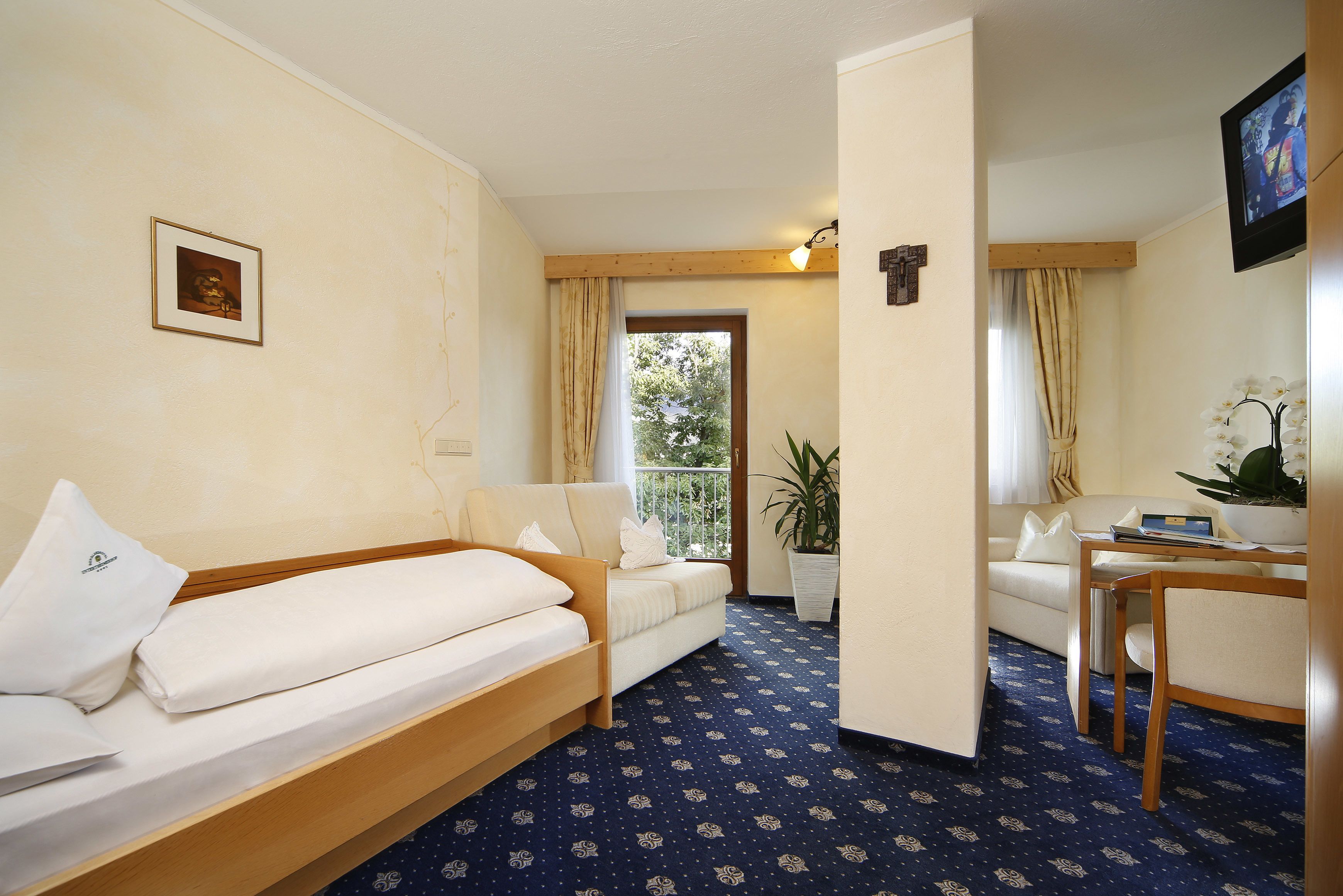 A hotel room with a bed, a sofa, a small table, and a potted plant.
