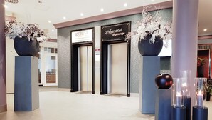 Een moderne lobby met een receptiebalie, twee grote vazen vol bloemen, en een bord met 'Clivia' en 'Agendblick'.