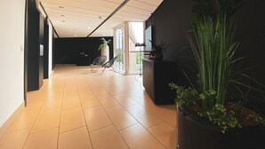 Een moderne gang met een betegelde vloer, een grote potplant en een zwarte wand.