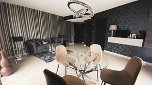 Een moderne woonkamer met een glazen salontafel, twee bruine stoelen, een zwarte bank en een decoratieve kroonluchter.