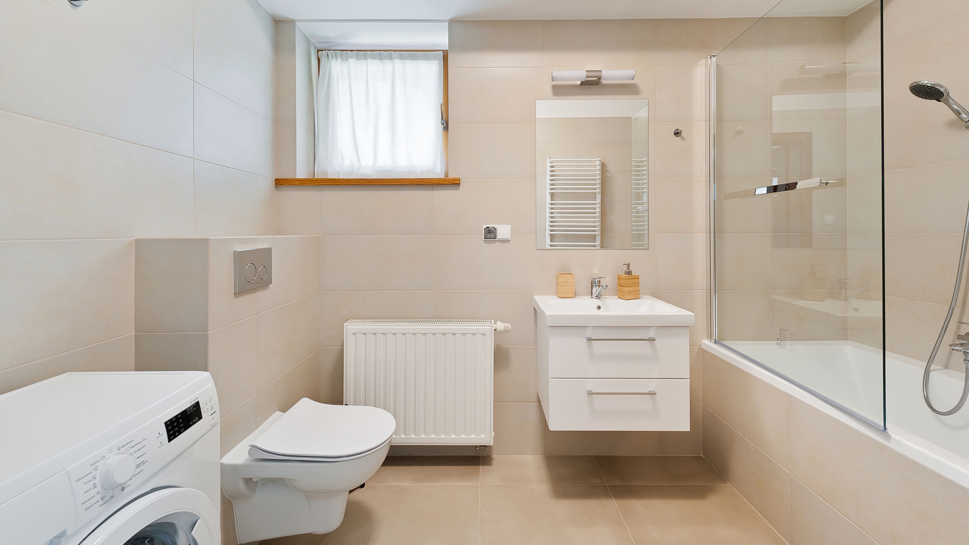 A compact bathroom with a toilet, washing machine, radiator, sink, and glass shower enclosure.