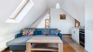 A modern loft apartment with a loft bed, a dining table, a kitchen with white cabinets, and a large window providing natural light. - Apartamenty Sun&Snow Lipki Park Zakopane (Zakopane)