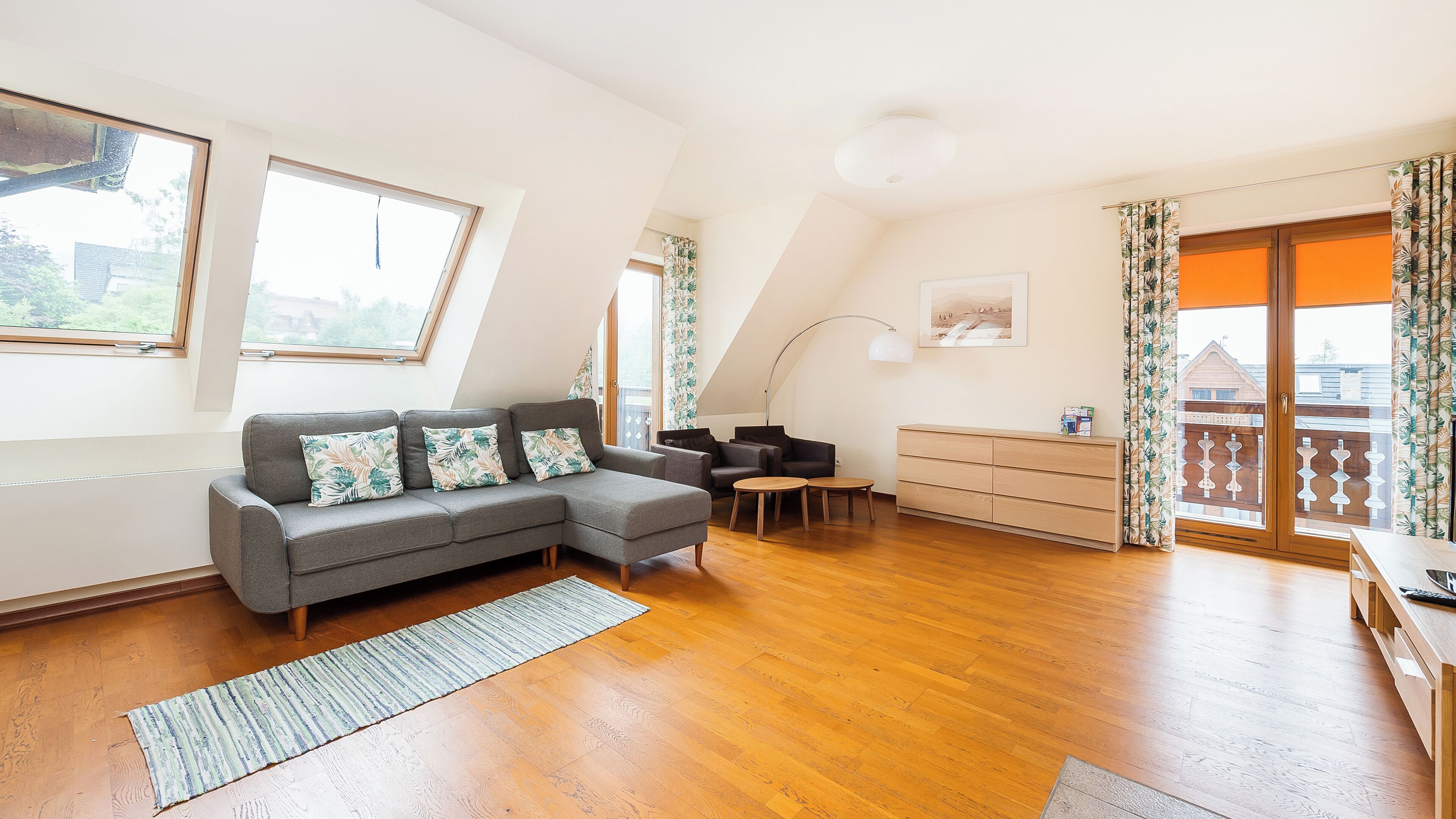 A modern living room with a grey sectional sofa, a wooden cabinet, and a dining area with two round tables.