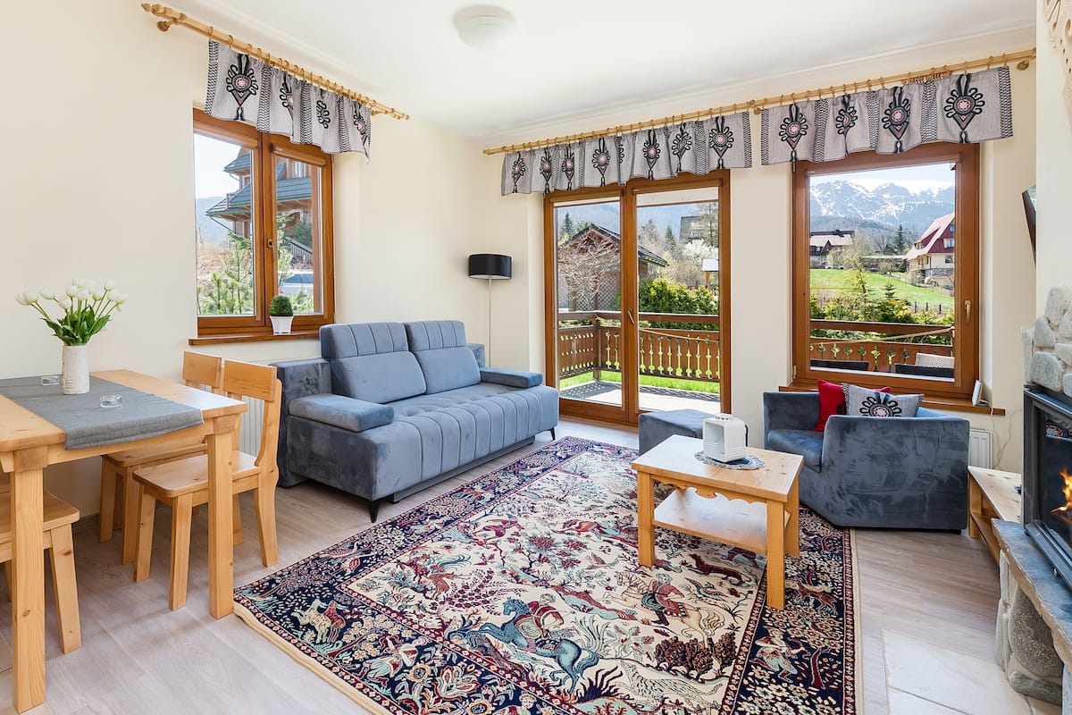 Una sala de estar acogedora con un sofá, una mesa de comedor con sillas, una chimenea y vistas al exterior.