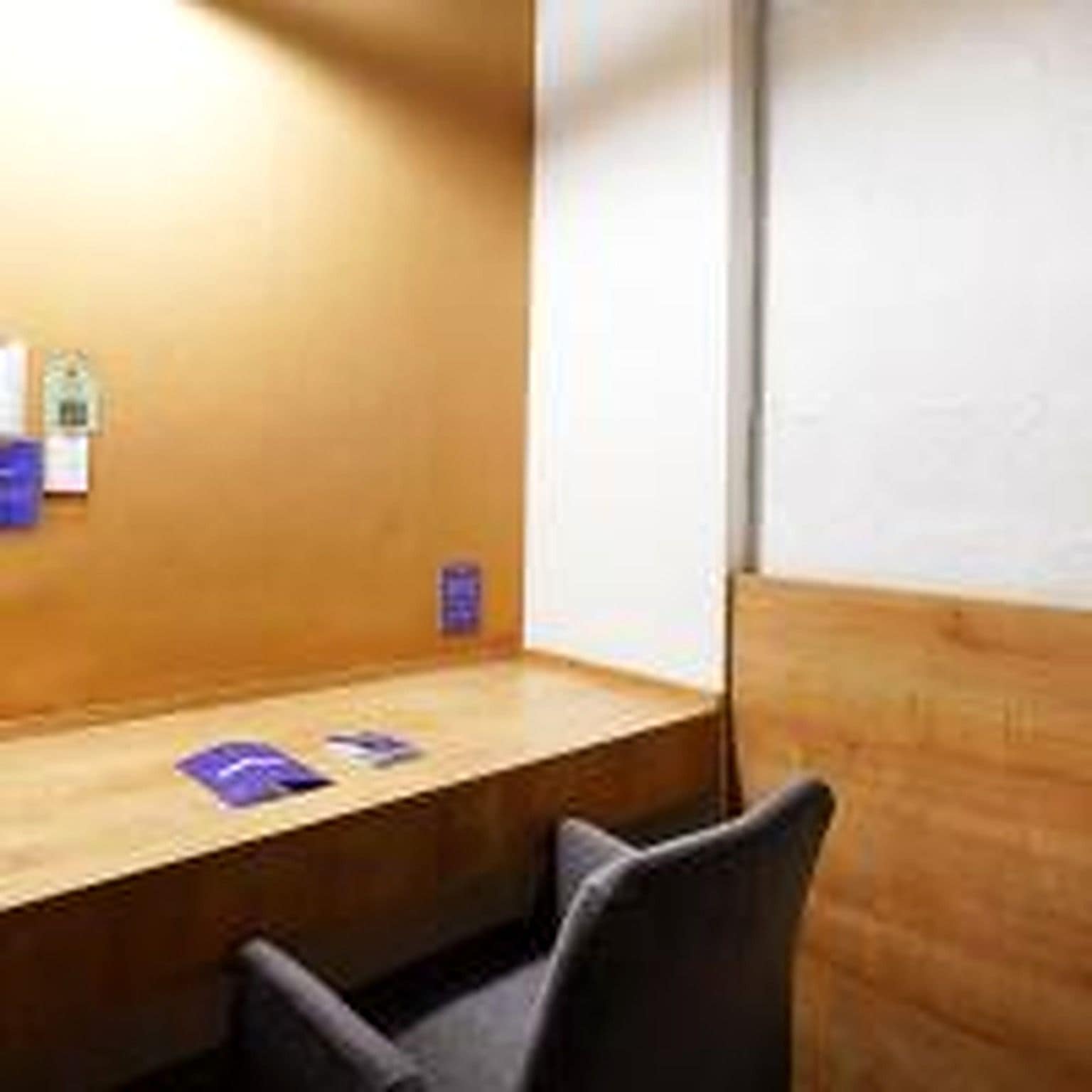 A wooden desk with a chair, a bulletin board with papers, and a small shelf with items.