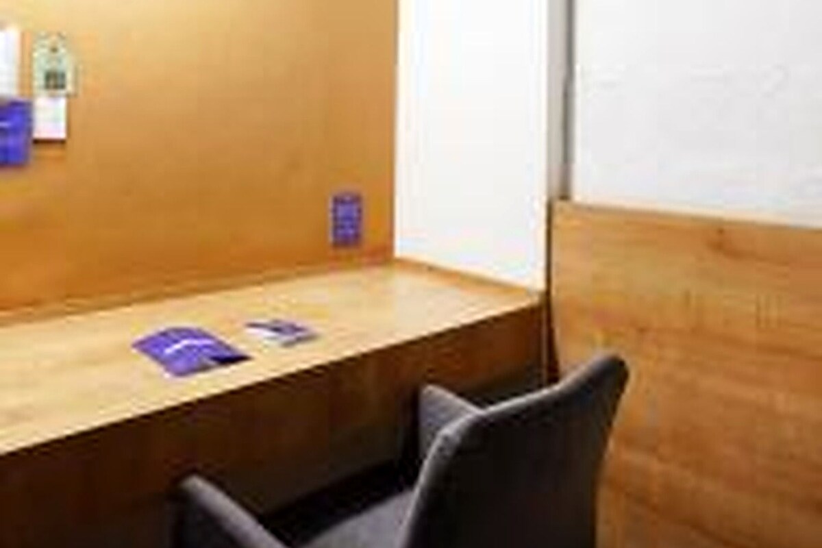 A wooden desk with a chair, a bulletin board with papers, and a small shelf with items.