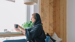 A person sitting by a window with a plant, holding a mug.
