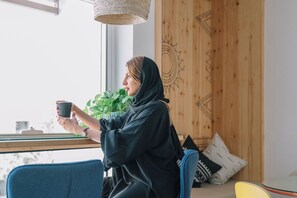 A person sitting by a window with a plant, holding a mug.