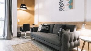 A modern living room with a grey sofa, a woven rug, a wooden desk, and a pendant light.