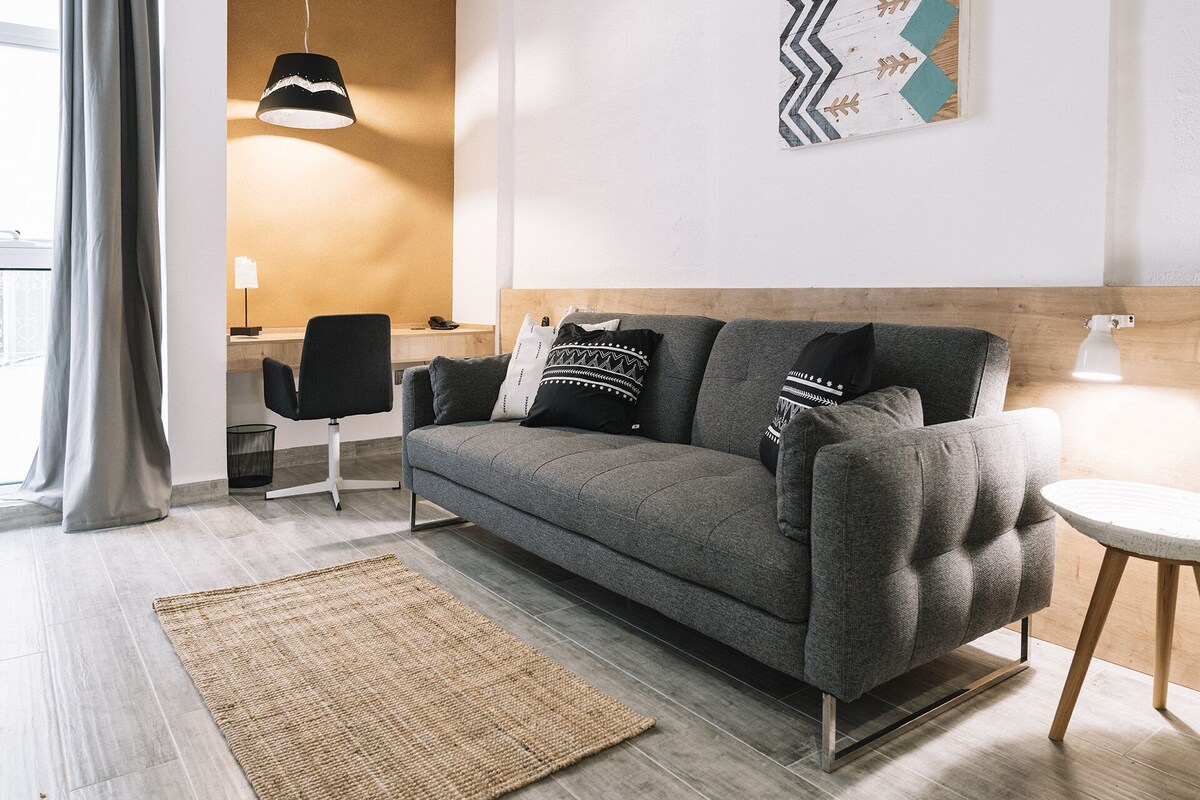 A modern living room with a grey sofa, a woven rug, a wooden desk, and a pendant light.
